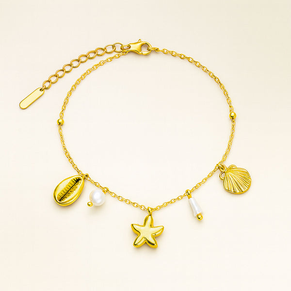 Gold bracelet with starfish, shell, and pearl charms on a beige background